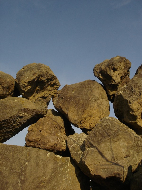 Cielo azul y piedras superiores de una cerca que delimita una parcela cerca del pueblo de Huiramba por la tarde.