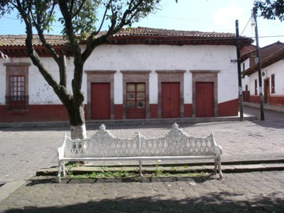 Fotograf�a donde aparecen parte de la portada de una casa que rodea la plaza, y tambi�n una banca blanca de la misma en el pueblo de Huiramba.